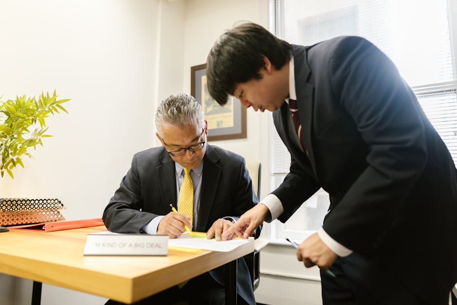 Two businessmen in suits collaborating on documents at an office desk, emphasizing teamwork.